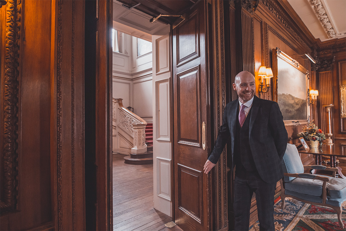 A man dressed smart suit opening huge wooden doors to a wonderful grand staircase at Knowsley Hall