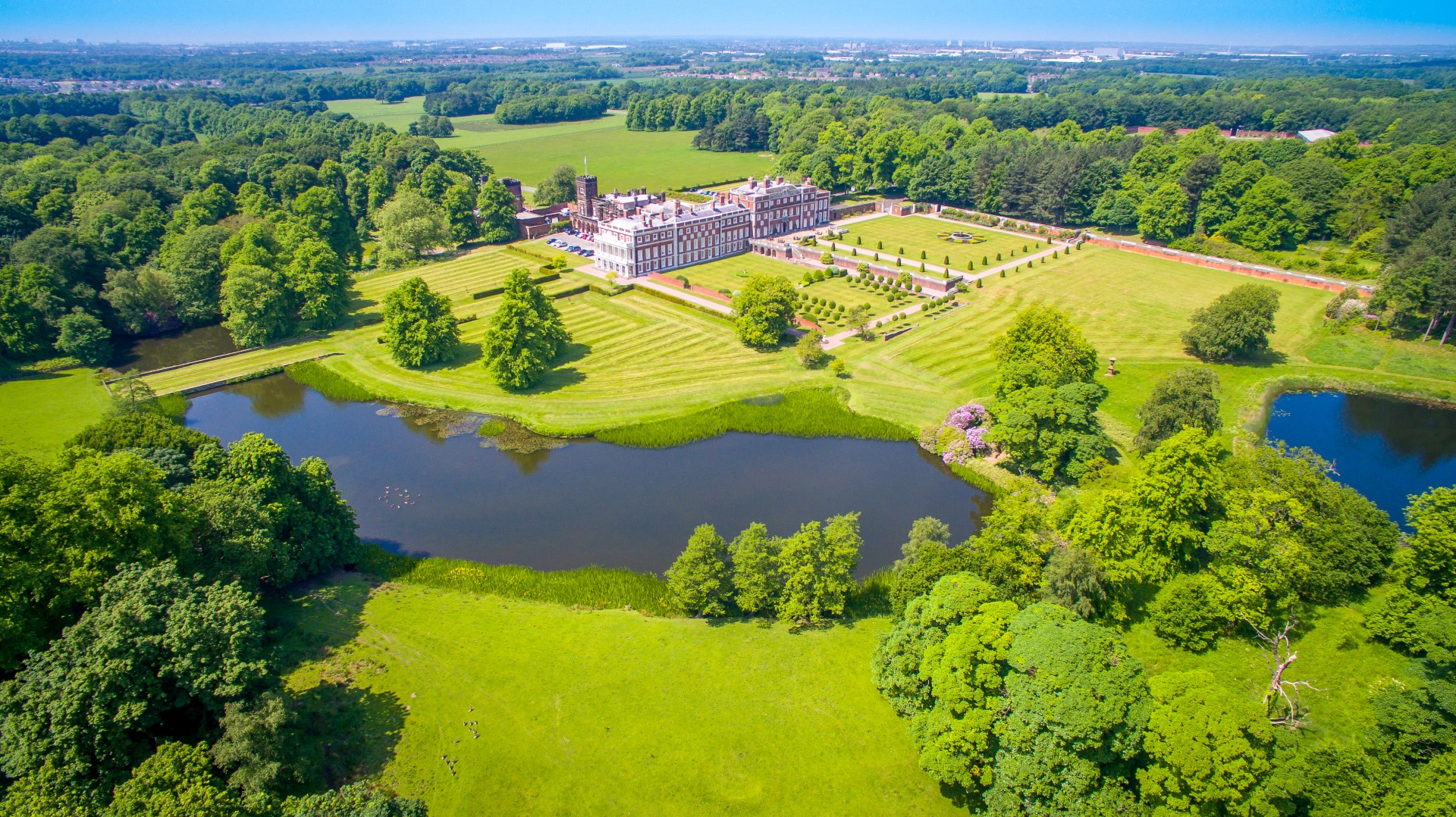 Birds eye view of a private estate with a stately home, extensive grounds and a lake