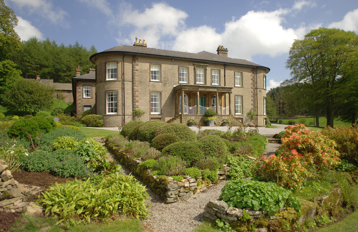 A beautiful country house set in stunning grounds with shrubs at the front of the house 