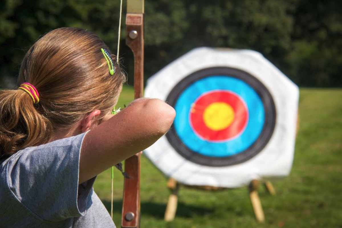 A woman with a bow and arrow ready to hit a target for a team building activity