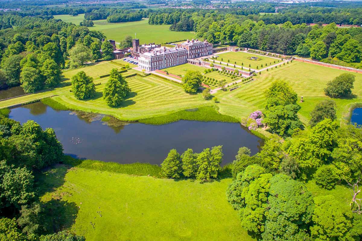 Aerial image of expansive manicured gardens, lake and large mansion house.