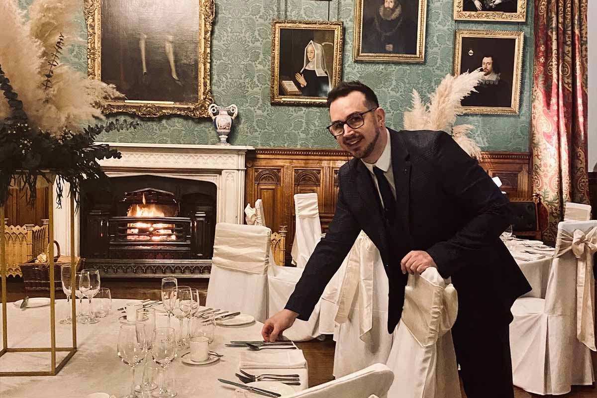 A man dressed formally in a suite at a table in the State Dining Room at Knowsley Hall