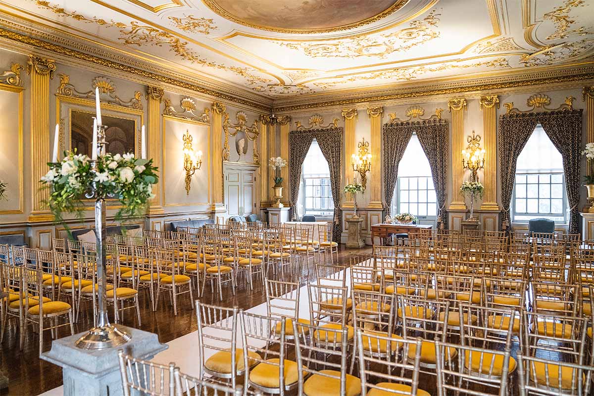 A beautiful ceremony room with gold ceiling and walls with gold chiavari Charis and wedding flowers at Knowsley Hal