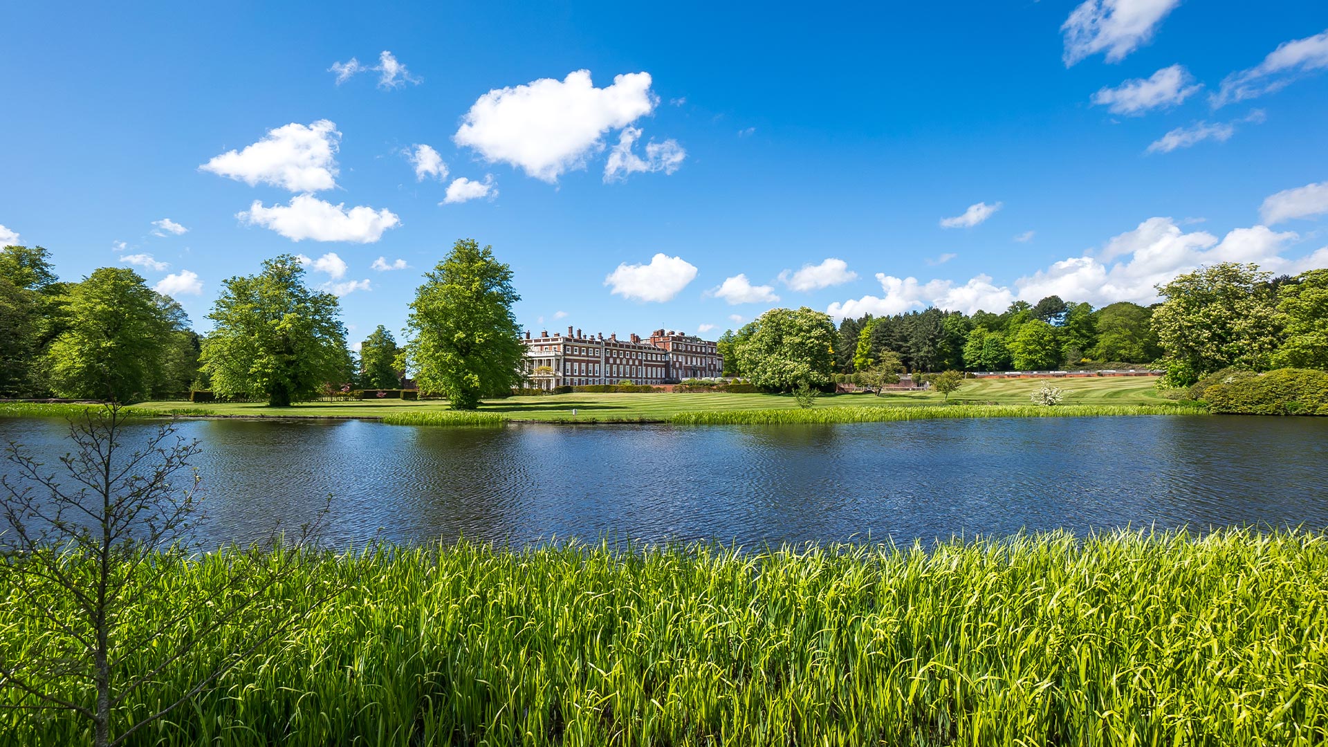 A lake overlooking a huge mansion house and gardens